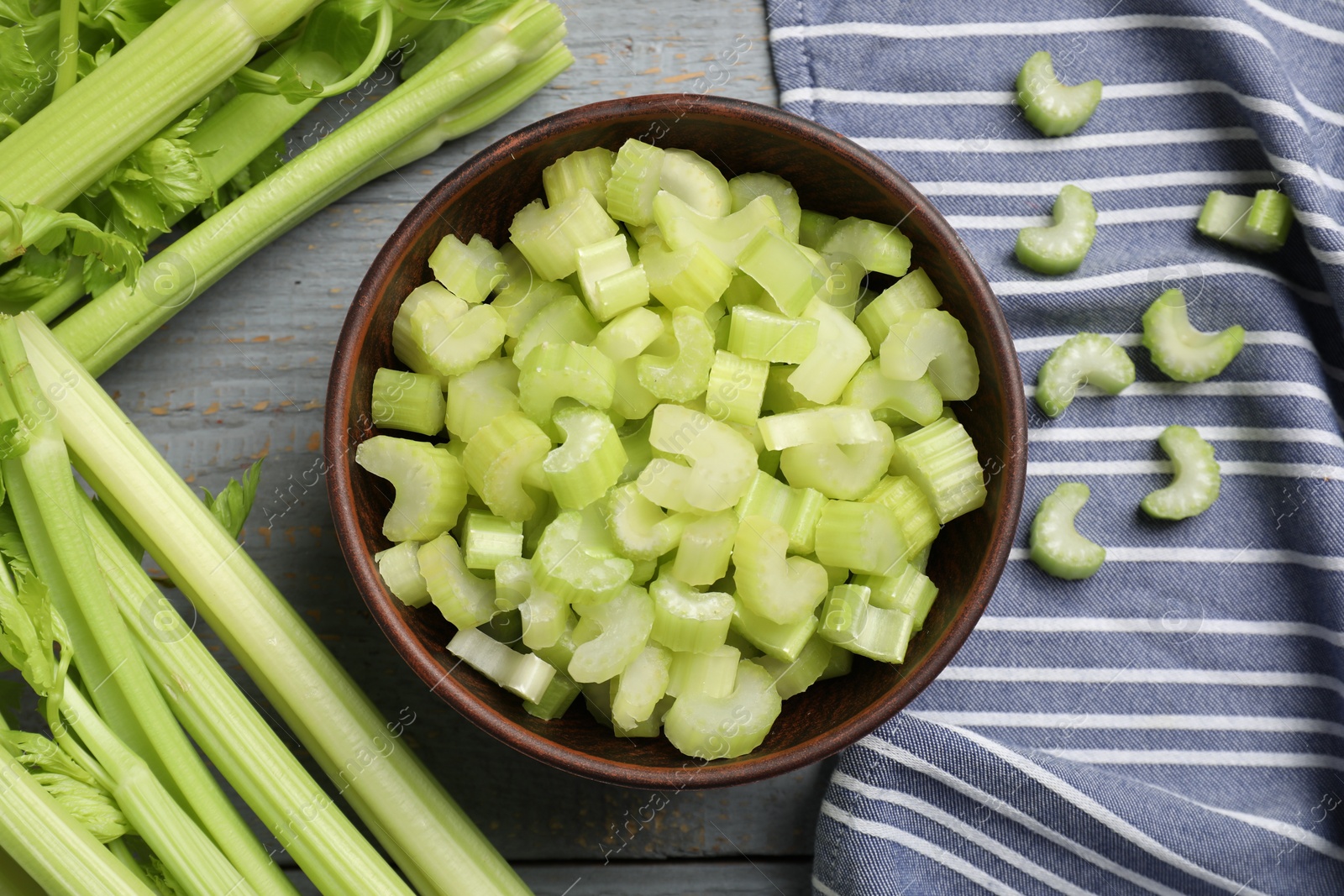 Photo of Fresh cut celery stalks in bowl and bunches on wooden table, flat lay