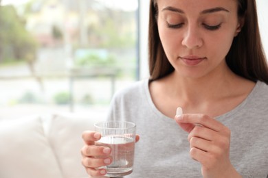 Photo of Young woman with glass of water taking pill at home, closeup