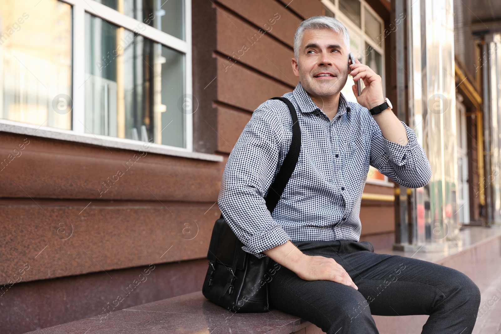Photo of Handsome businessman talking by mobile phone in city