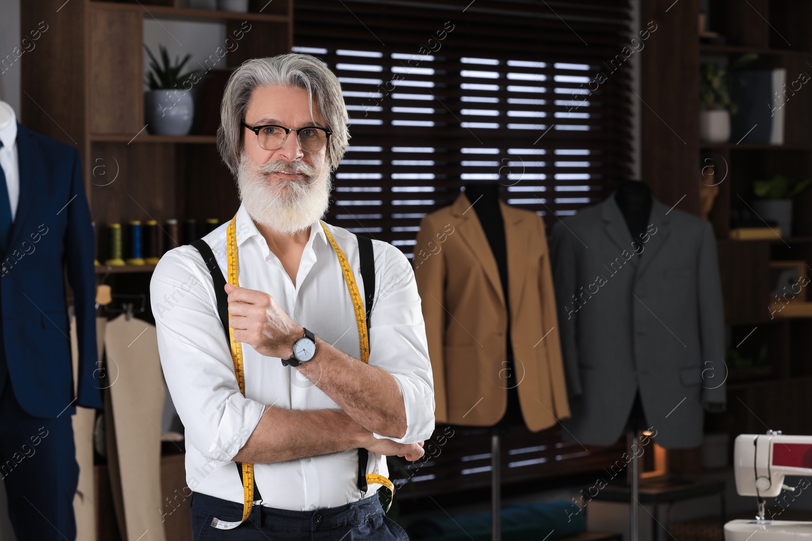 Photo of Professional tailor with measuring tape in workshop, space for text