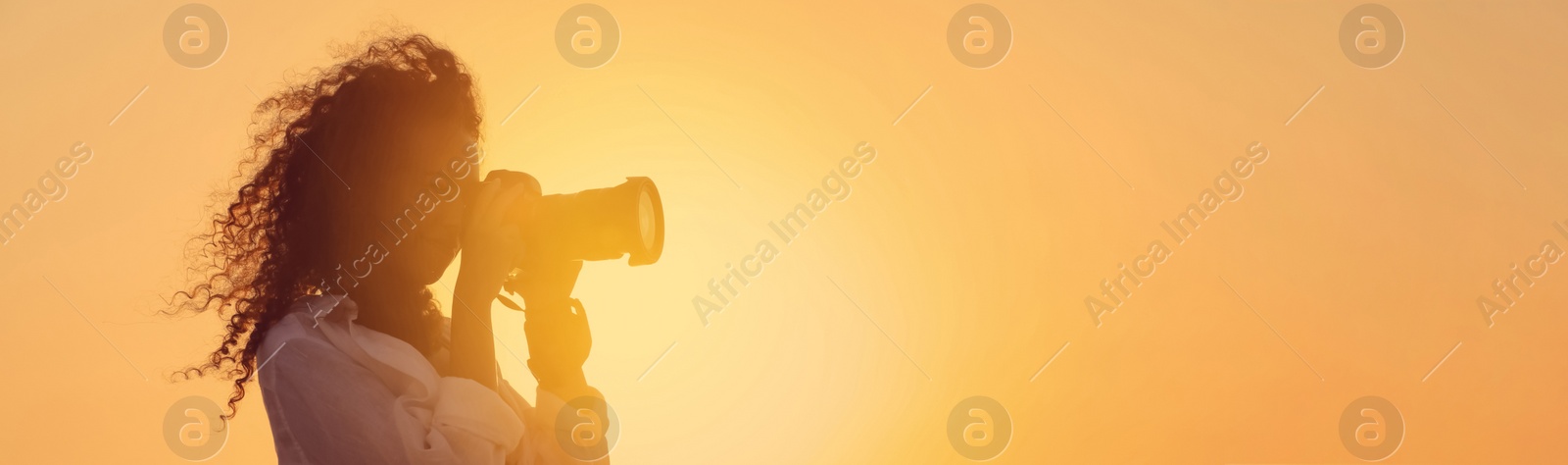 Image of African American photographer taking photo with professional camera outdoors at sunset, space for text. Banner design