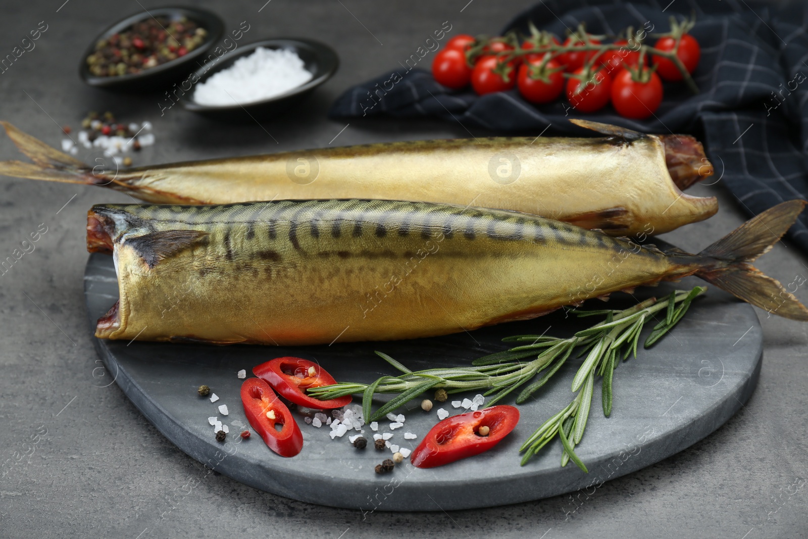 Photo of Delicious smoked mackerels and spices on dark grey table, closeup