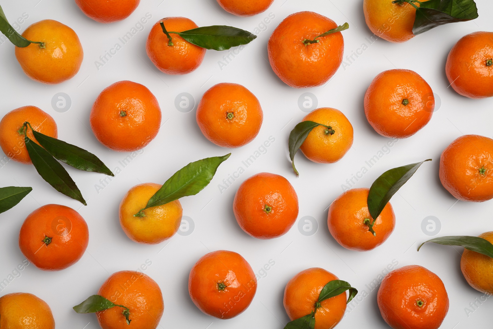 Photo of Delicious tangerines and green leaves on white background, flat lay