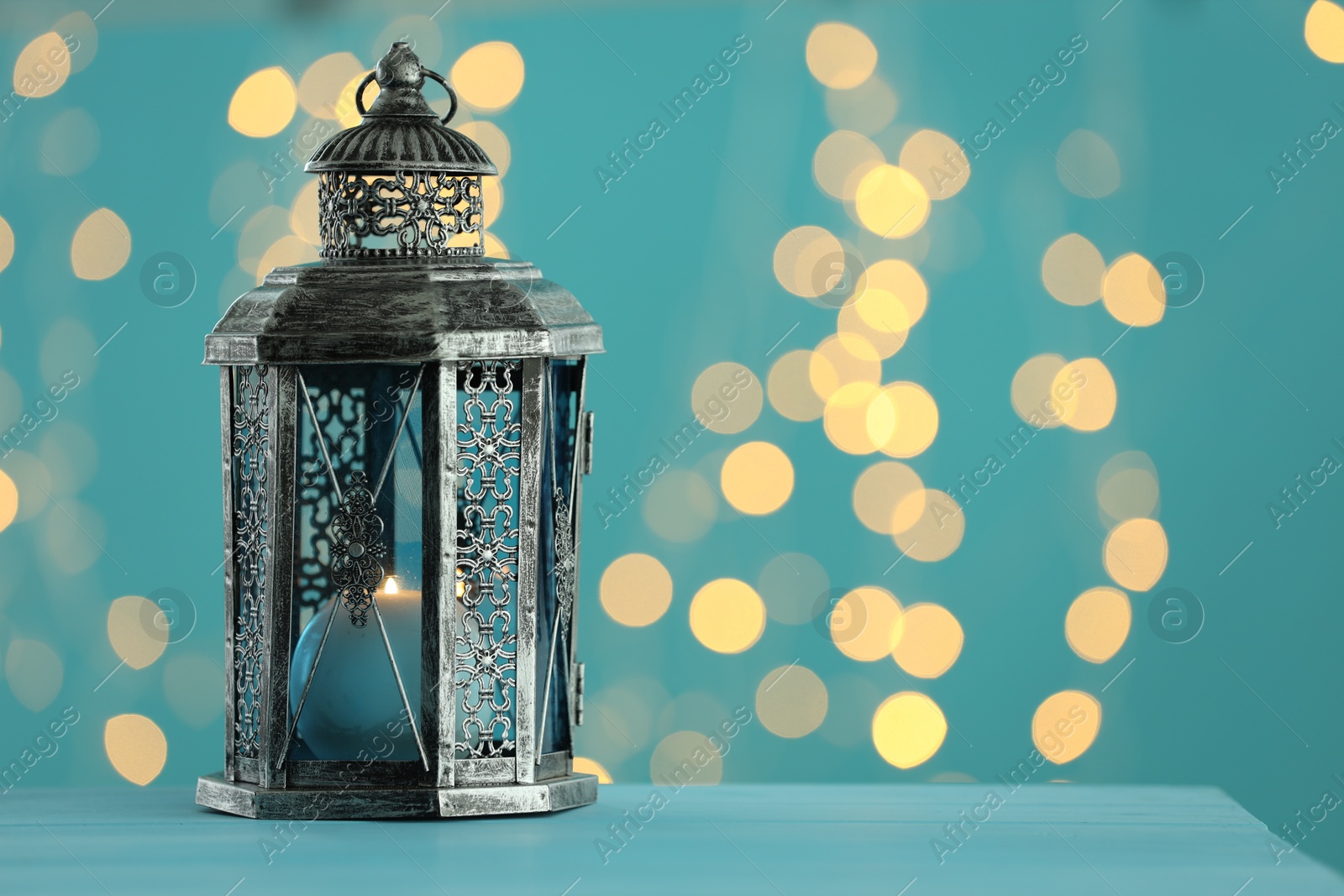 Photo of Traditional Arabic lantern on table against light blue background with blurred lights. Space for text