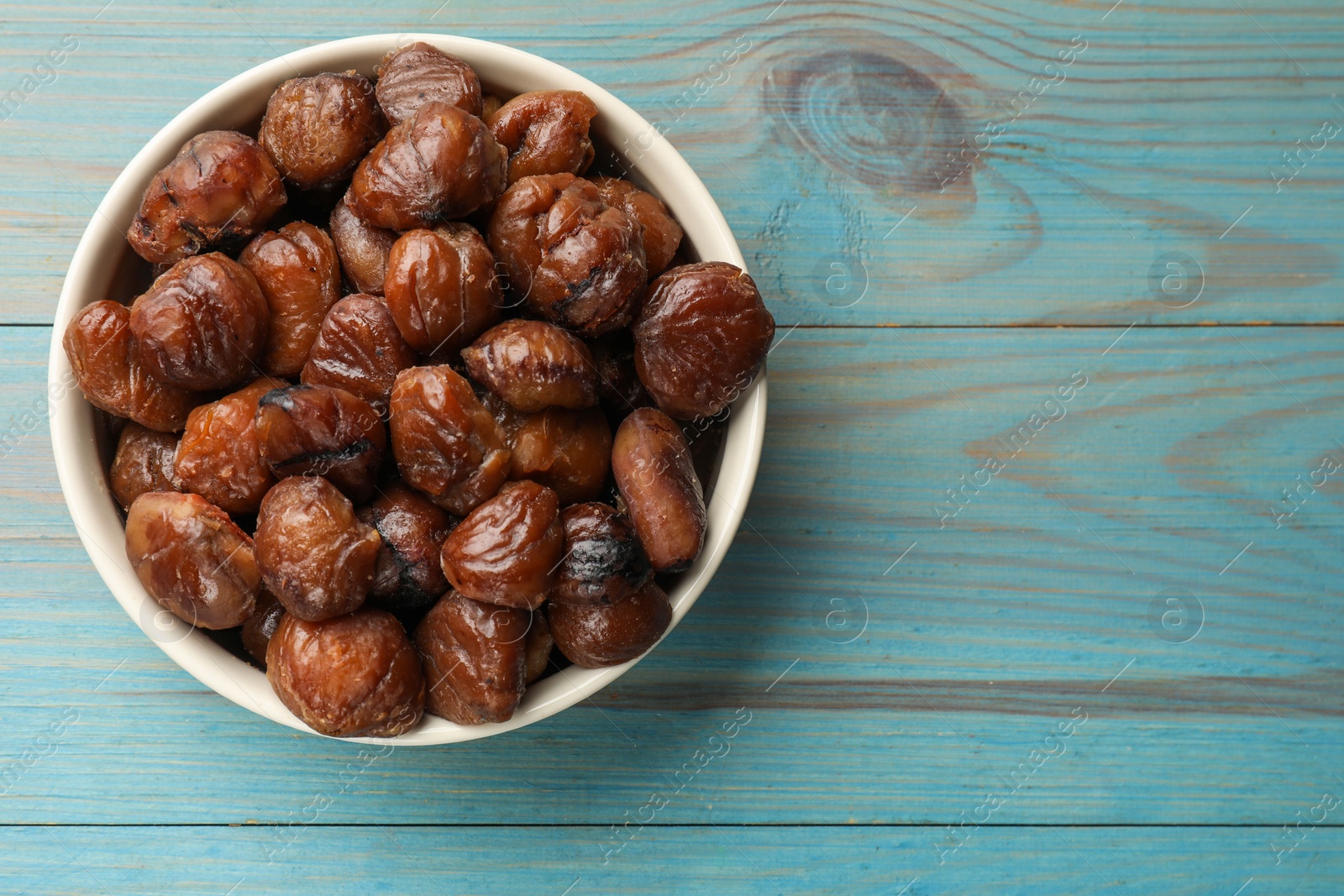 Photo of Roasted edible sweet chestnuts in bowl on light blue wooden table, top view. Space for text