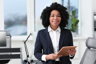 Photo of Smiling young businesswoman using tablet in office