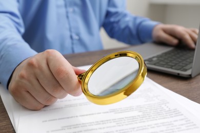 Man looking at document through magnifier at wooden table, closeup. Searching concept
