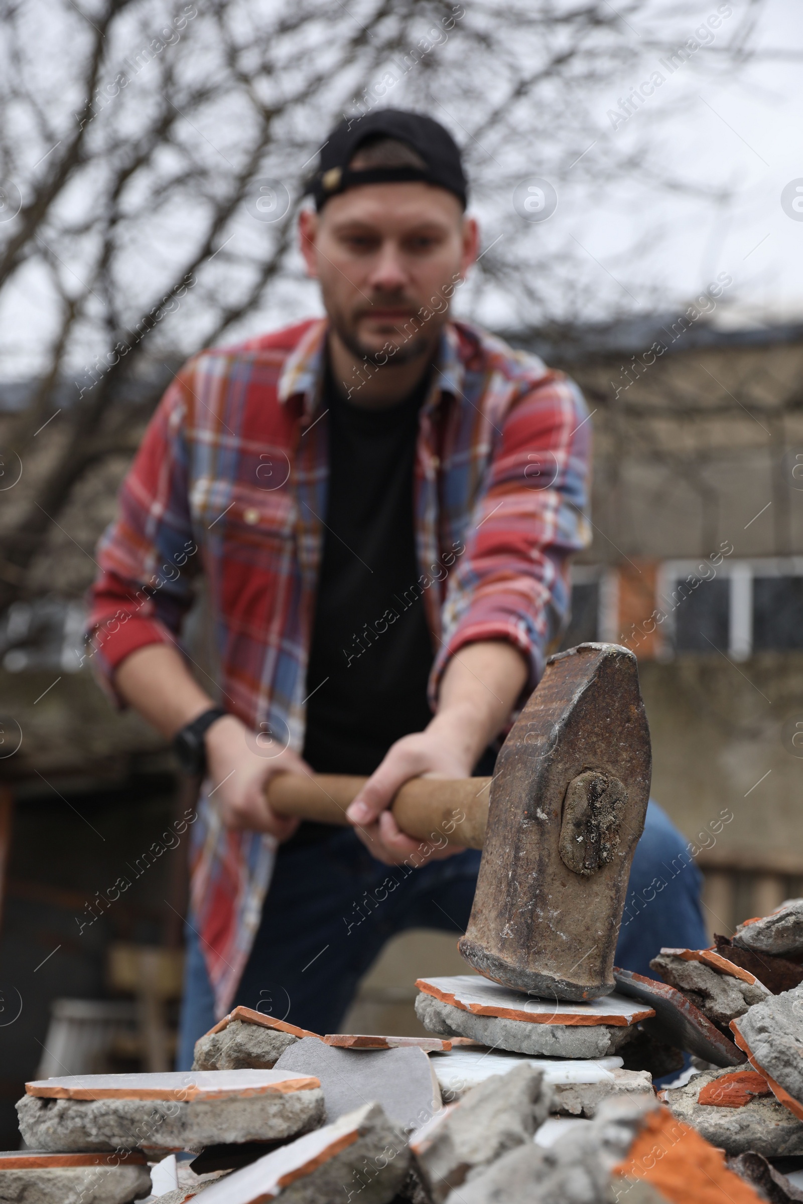 Photo of Man breaking bricks with sledgehammer outdoors, selective focus