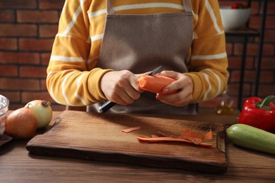 Photo of Woman peeling fresh carrot with knife at wooden table indoors, closeup