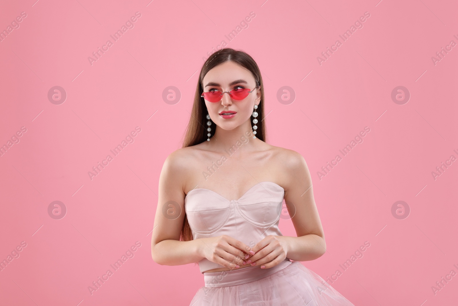 Photo of Pink look. Beautiful woman in dress and bright sunglasses on color background