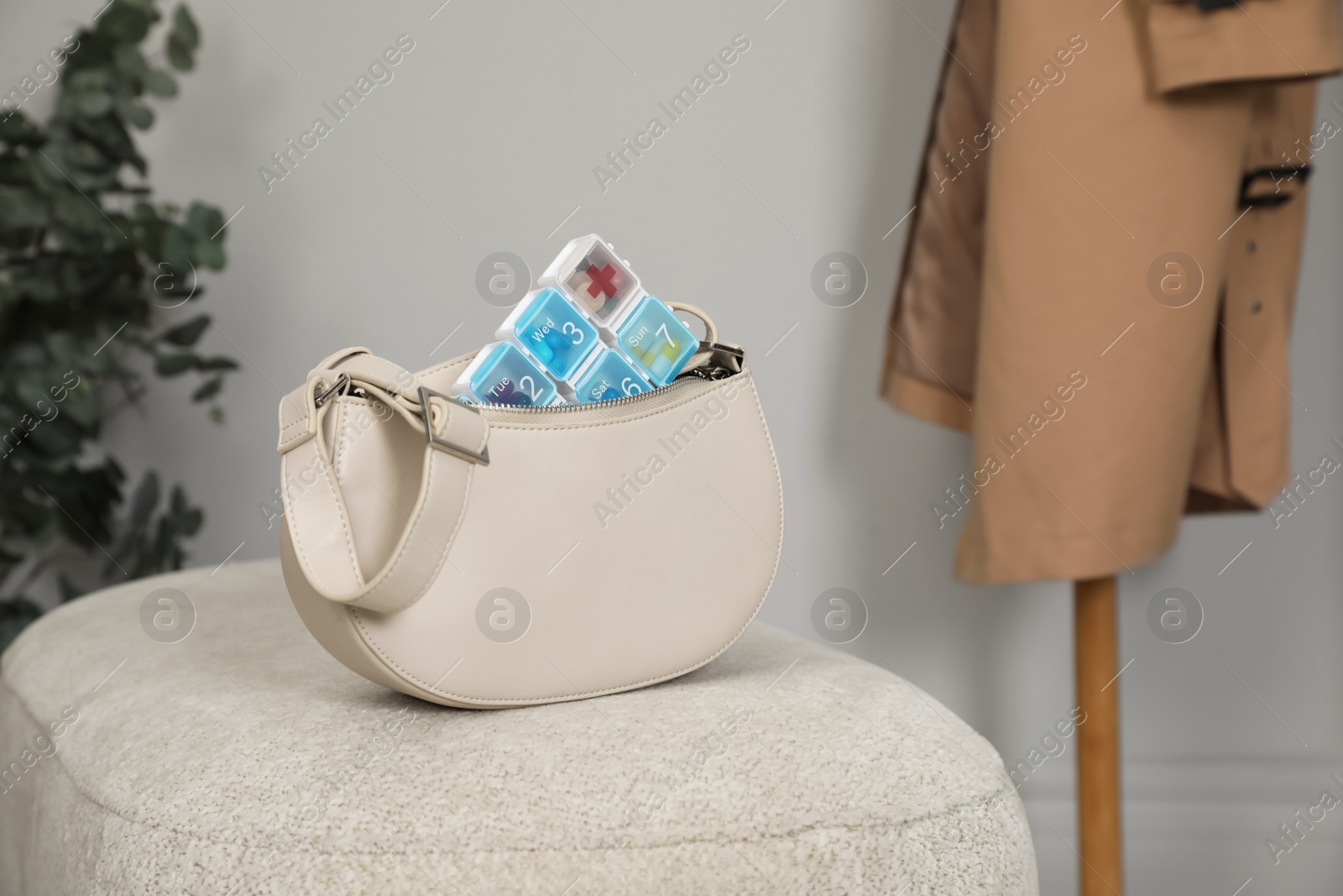 Photo of Stylish women's bag with plastic pill box on pouf indoors. Space for text