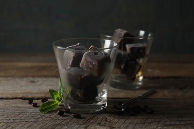 Photo of Glass of iced coffee cubes, beans and mint on wooden table, space for text