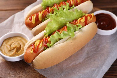 Photo of Tasty hot dogs with lettuce, ketchup and mustard on board, closeup