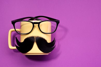 Man's face made of artificial mustache, cup and glasses on purple background, top view. Space for text