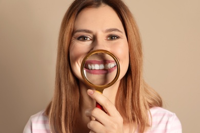 Photo of Smiling woman with perfect teeth and magnifier on color background, closeup
