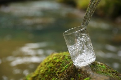 Fresh water pouring into glass on stone with moss near river. Space for text