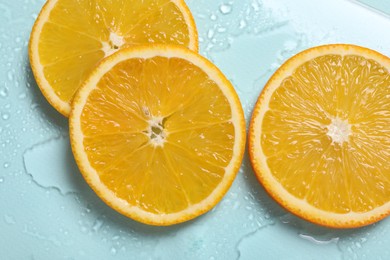 Slices of juicy orange and water on light blue background, top view