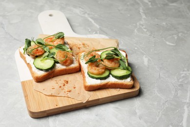 Photo of Tasty toasts with cream cheese, shrimps, cucumbers and microgreens served on grey marble table