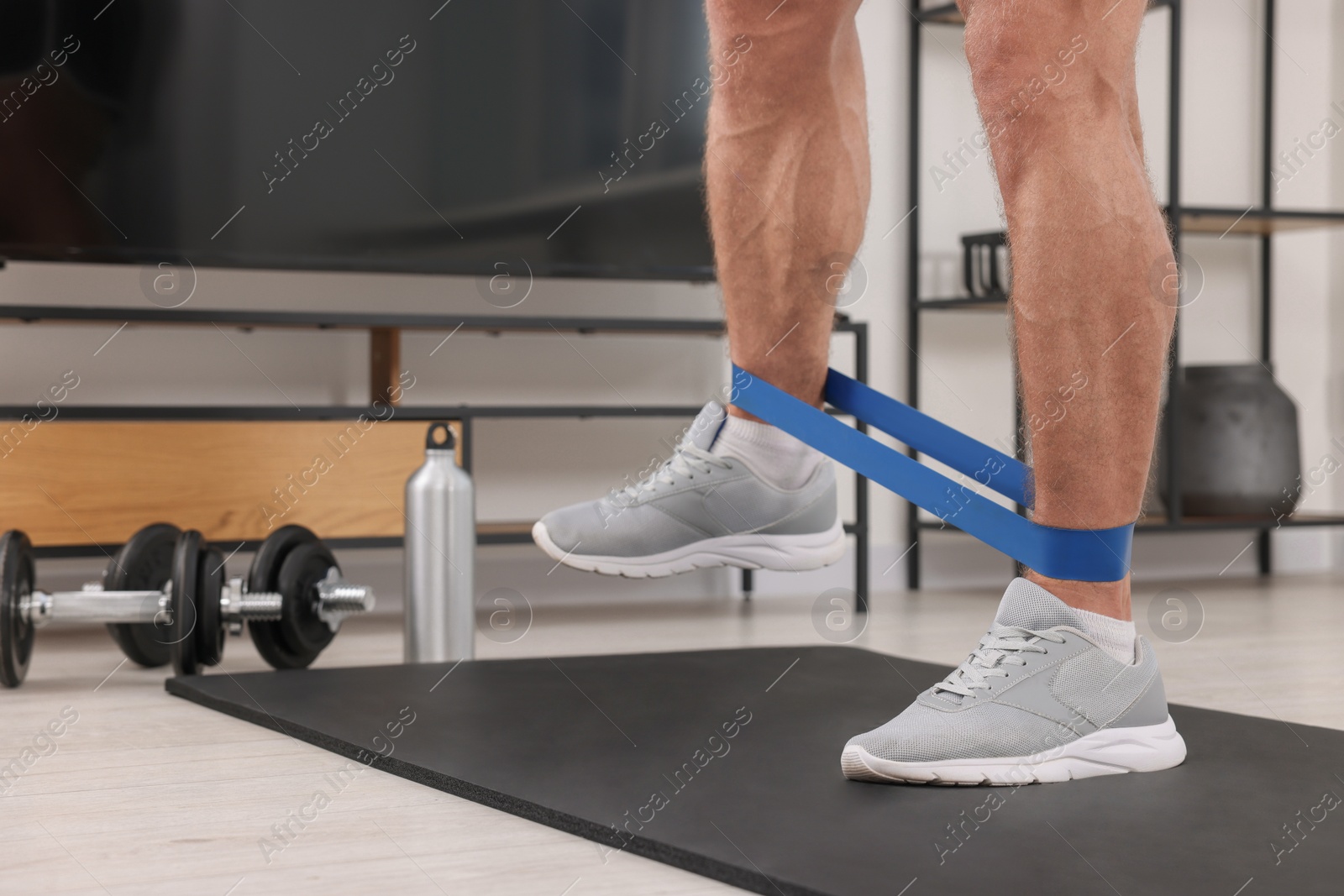 Photo of Athletic man doing exercise with elastic resistance band on mat at home, closeup