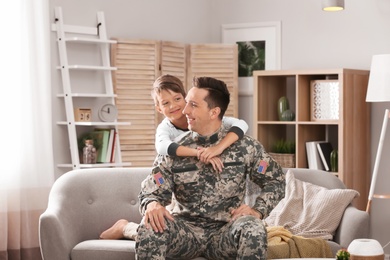 Young man in military uniform with his little son on sofa at home