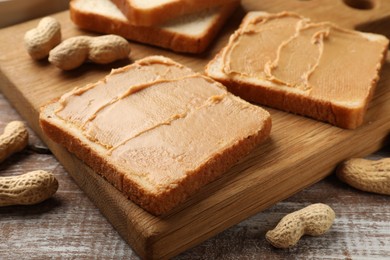 Photo of Tasty peanut butter sandwiches and peanuts on wooden table, closeup