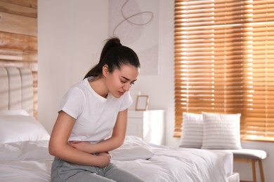 Photo of Young woman suffering from stomach ache on bed at home. Food poisoning