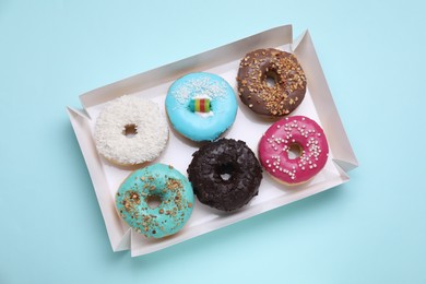 Photo of Box with different tasty glazed donuts on light blue background, top view