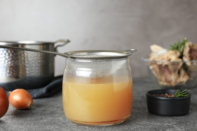 Glass jar with delicious bone broth and sieve on grey table