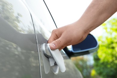 Man with napkin sanitizing car door handle outdoors, closeup