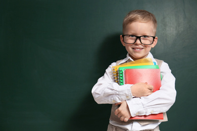 Photo of Cute little child wearing glasses near chalkboard, space for text. First time at school