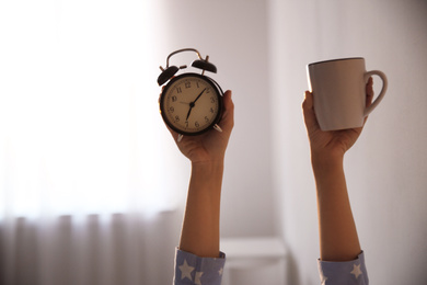 Photo of Woman with cup and alarm clock at home, closeup. Morning time