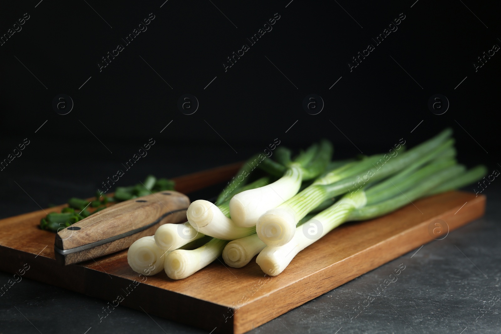 Photo of Fresh green spring onions and knife on wooden board, closeup