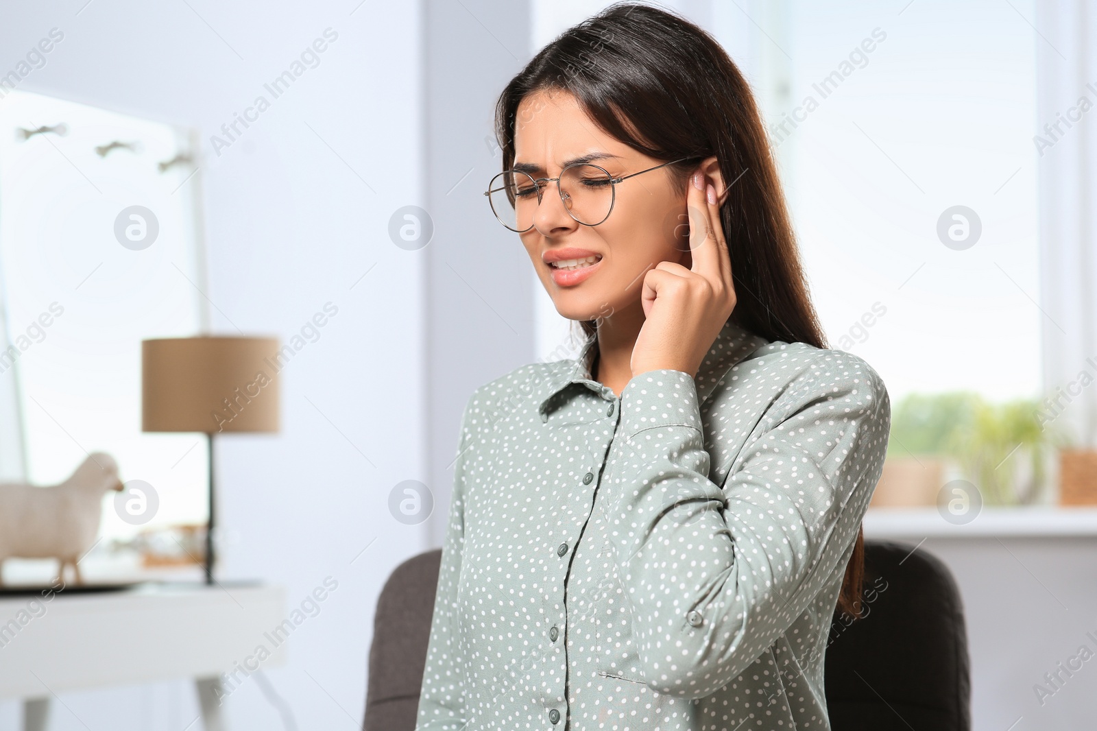 Photo of Young woman in eyeglasses suffering from ear pain indoors