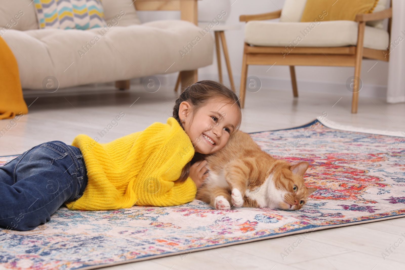 Photo of Happy little girl and cute ginger cat on carpet at home