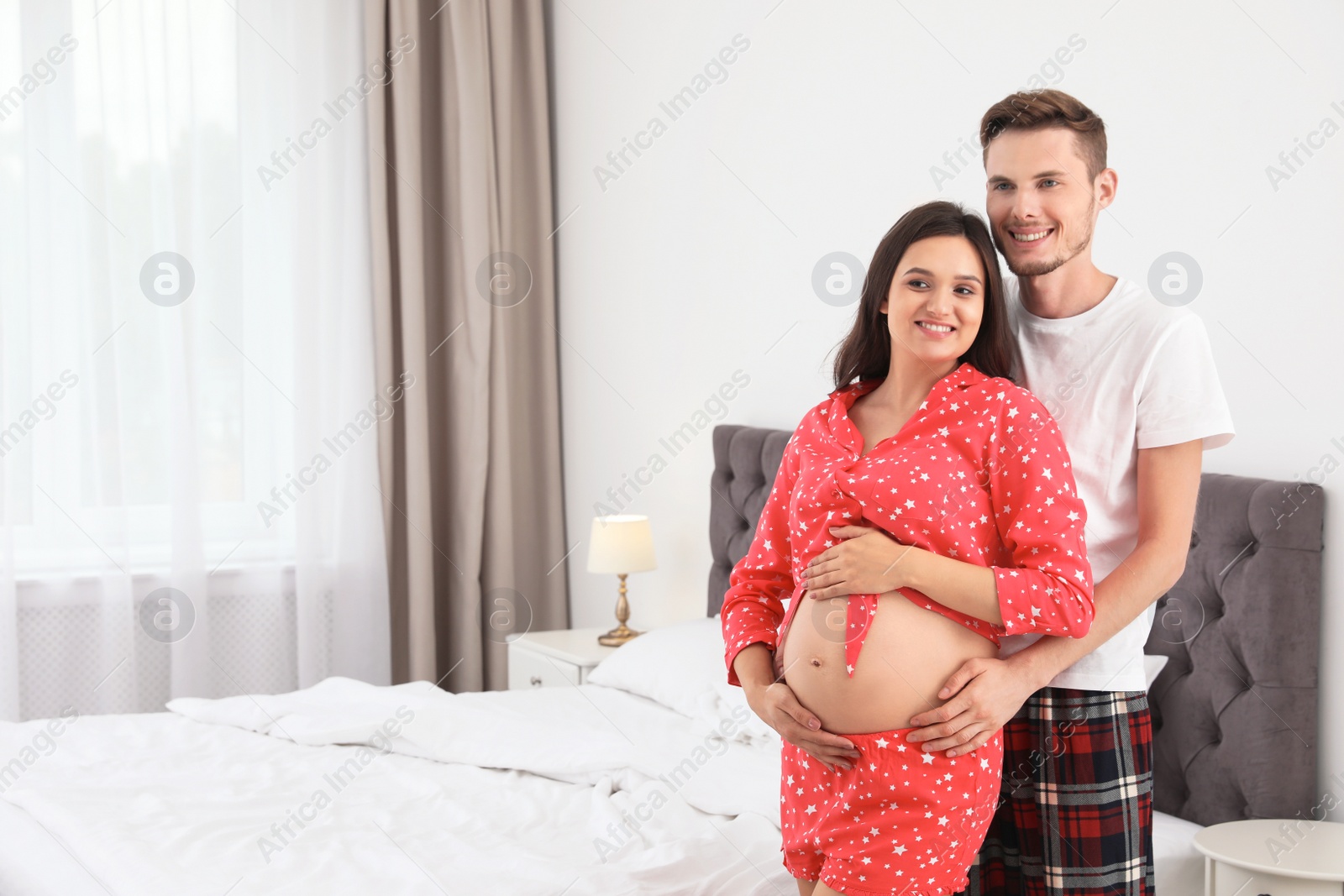 Photo of Young husband hugging his lovely pregnant wife in bedroom. Space for text