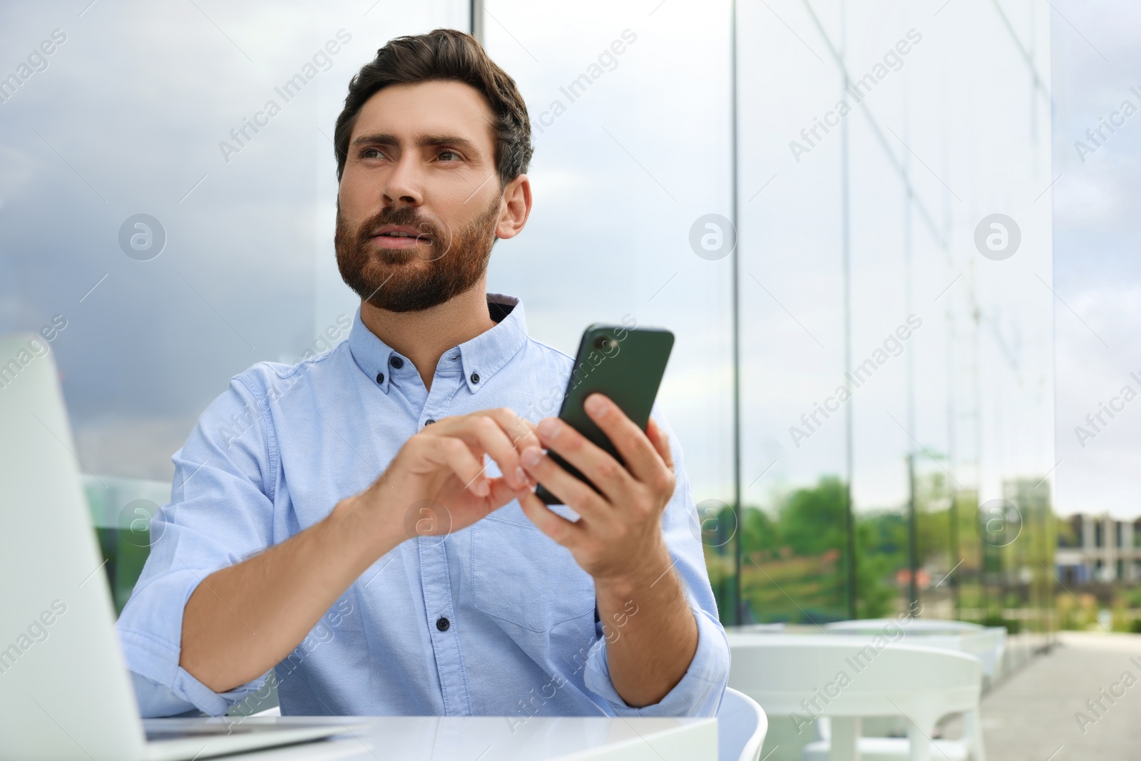 Photo of Handsome man with smartphone and laptop in outdoor cafe, space for text