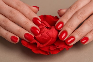 Photo of Woman with red polish on nails touching flower on beige background, closeup