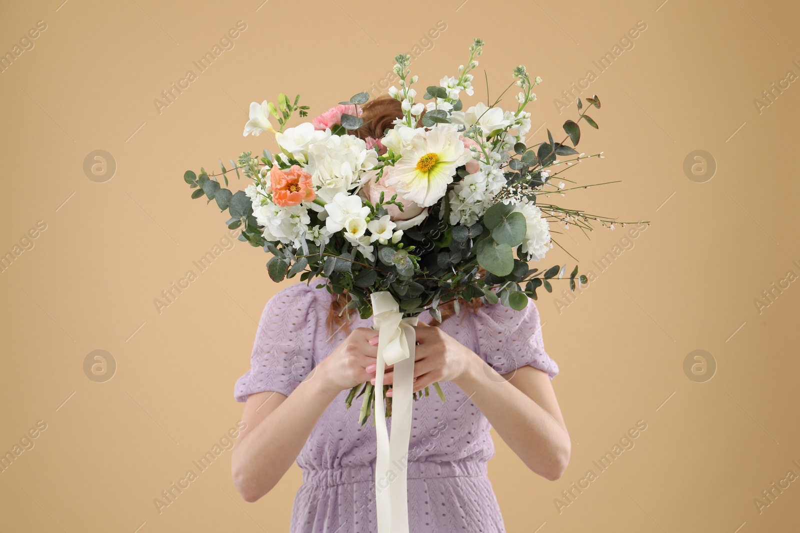 Photo of Woman covering her face with bouquet of beautiful flowers on beige background