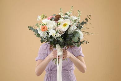 Photo of Woman covering her face with bouquet of beautiful flowers on beige background