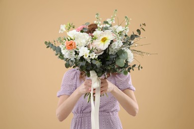 Woman covering her face with bouquet of beautiful flowers on beige background