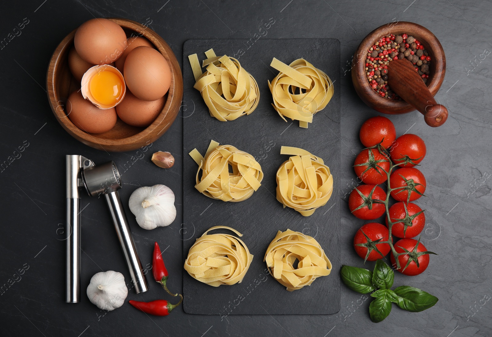 Photo of Flat lay composition with uncooked tagliatelle and fresh ingredients on black table