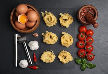 Flat lay composition with uncooked tagliatelle and fresh ingredients on black table