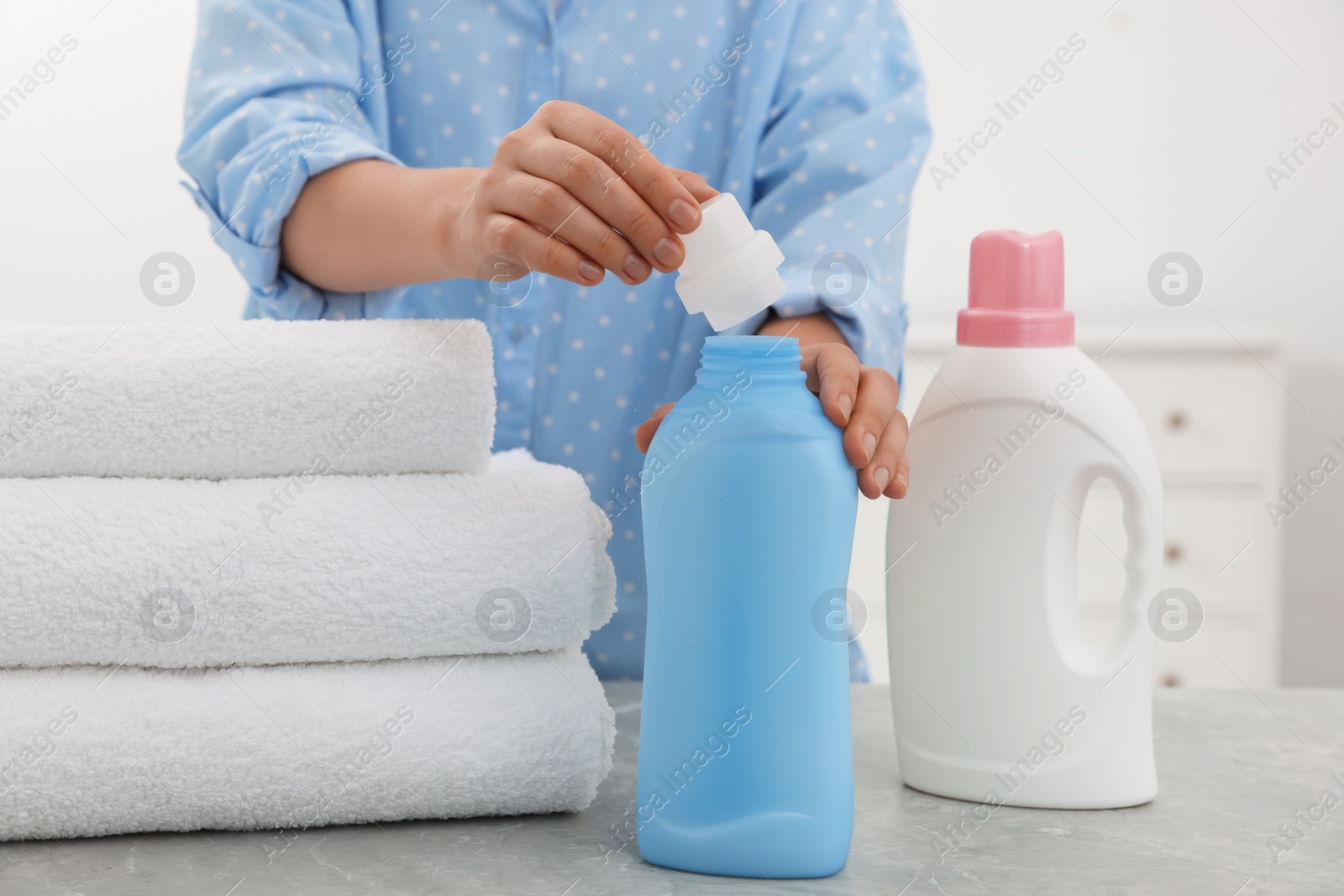 Photo of Woman opening bottle of laundry detergent at light grey marble table, closeup