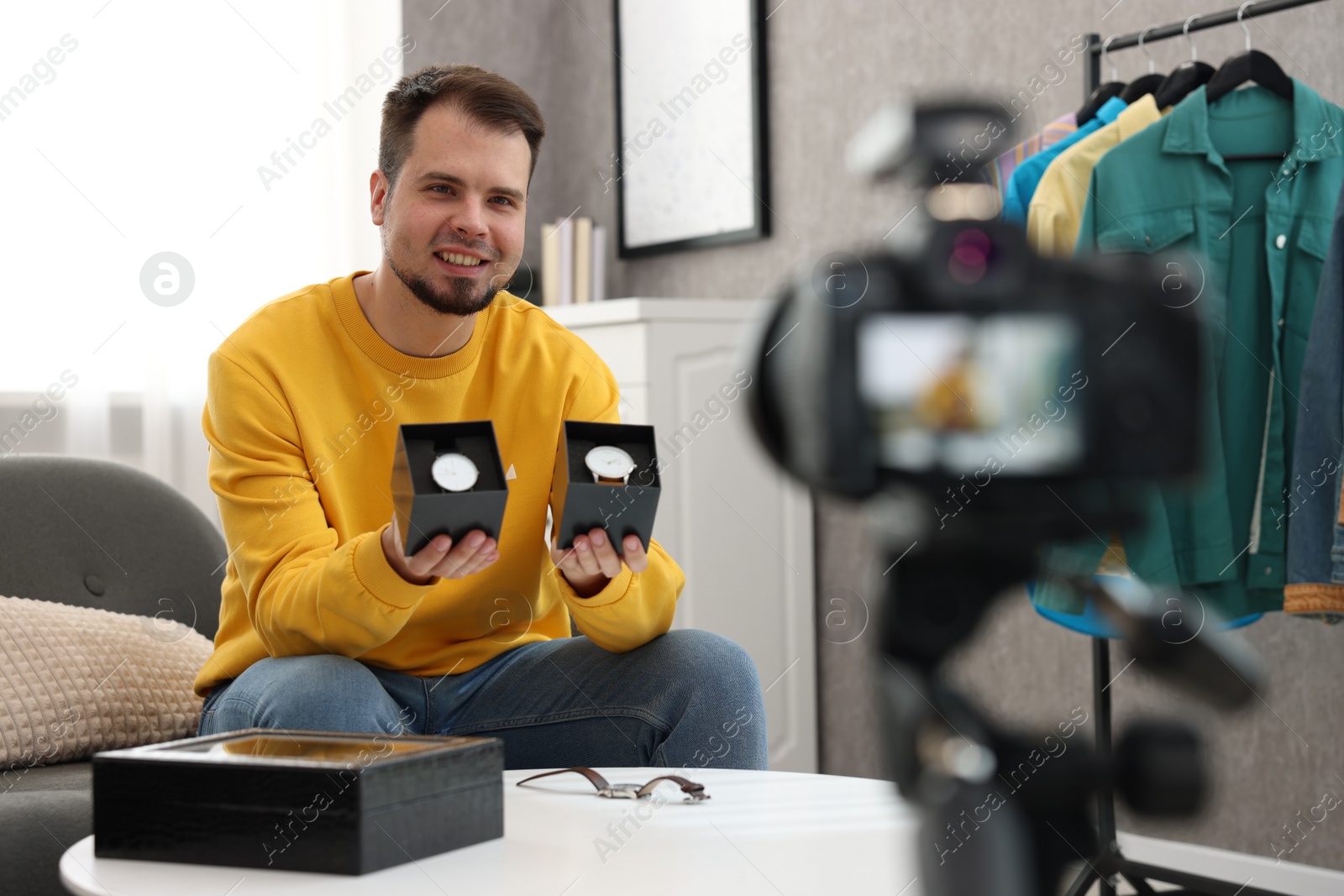 Photo of Smiling fashion blogger showing wristwatches while recording video at home