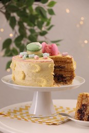 Photo of Delicious cake decorated with macarons and marshmallows on white table against blurred lights