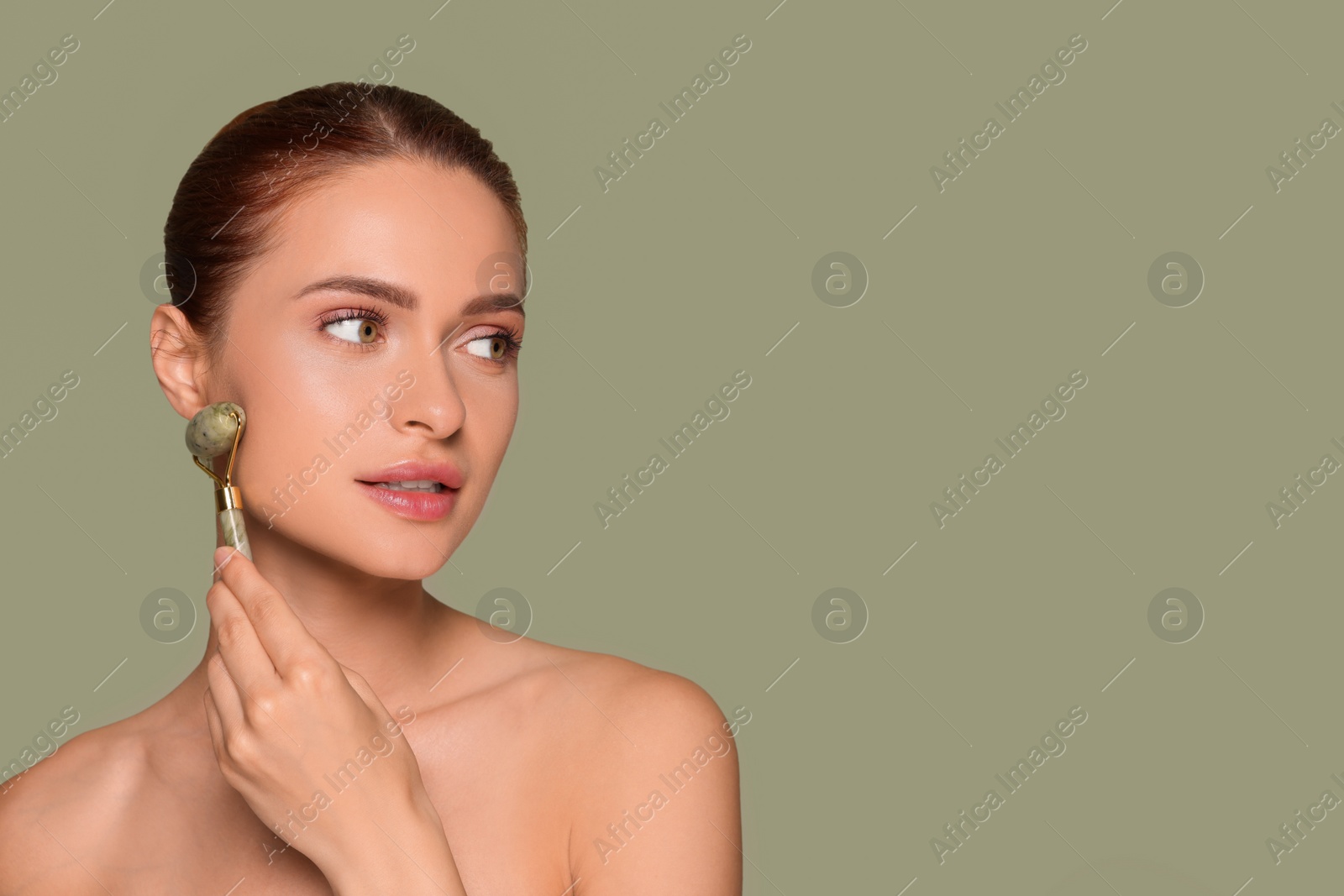 Photo of Young woman massaging her face with jade roller on green background, space for text