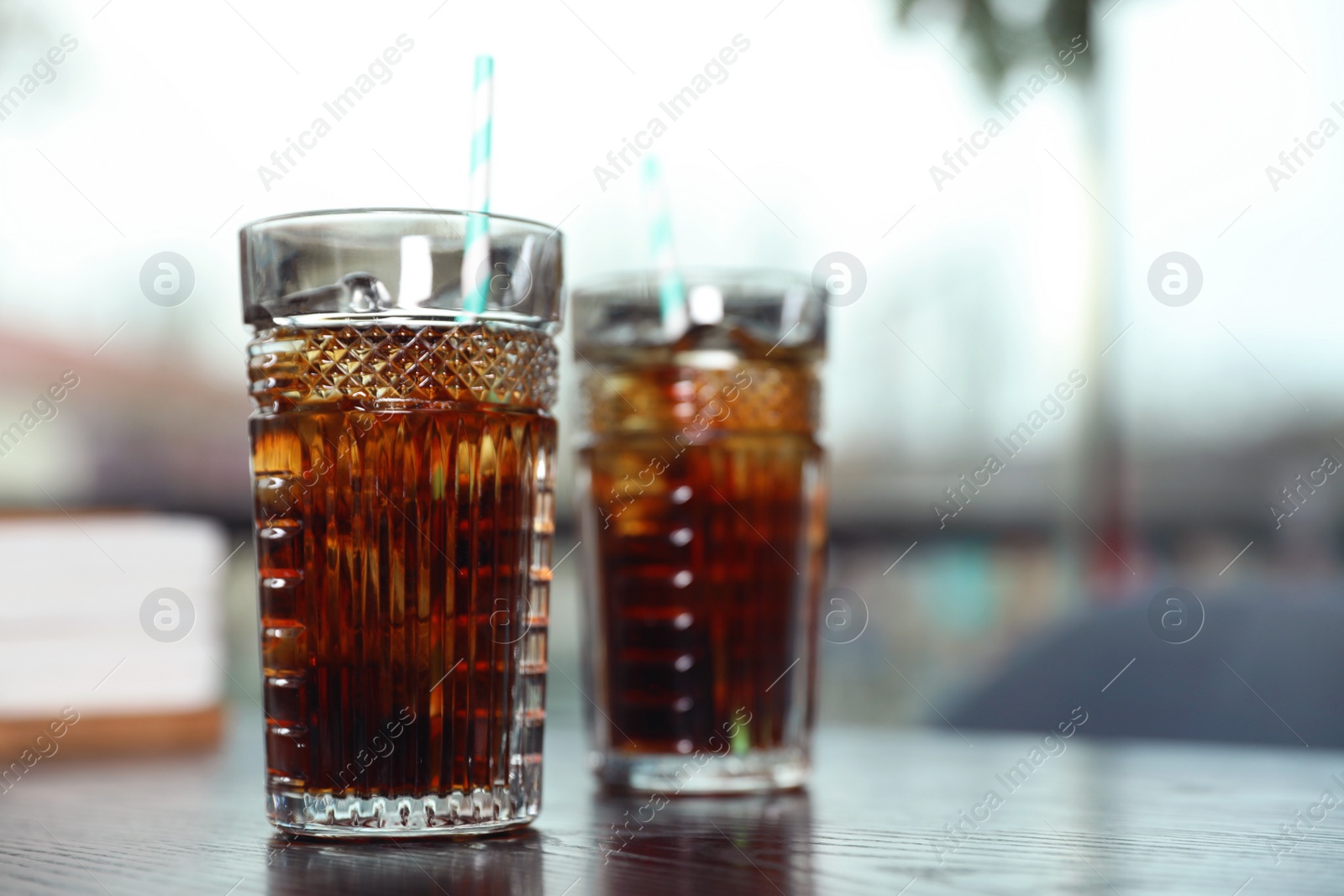 Photo of Glasses with refreshing cola and ice cubes on table indoors. Space for text