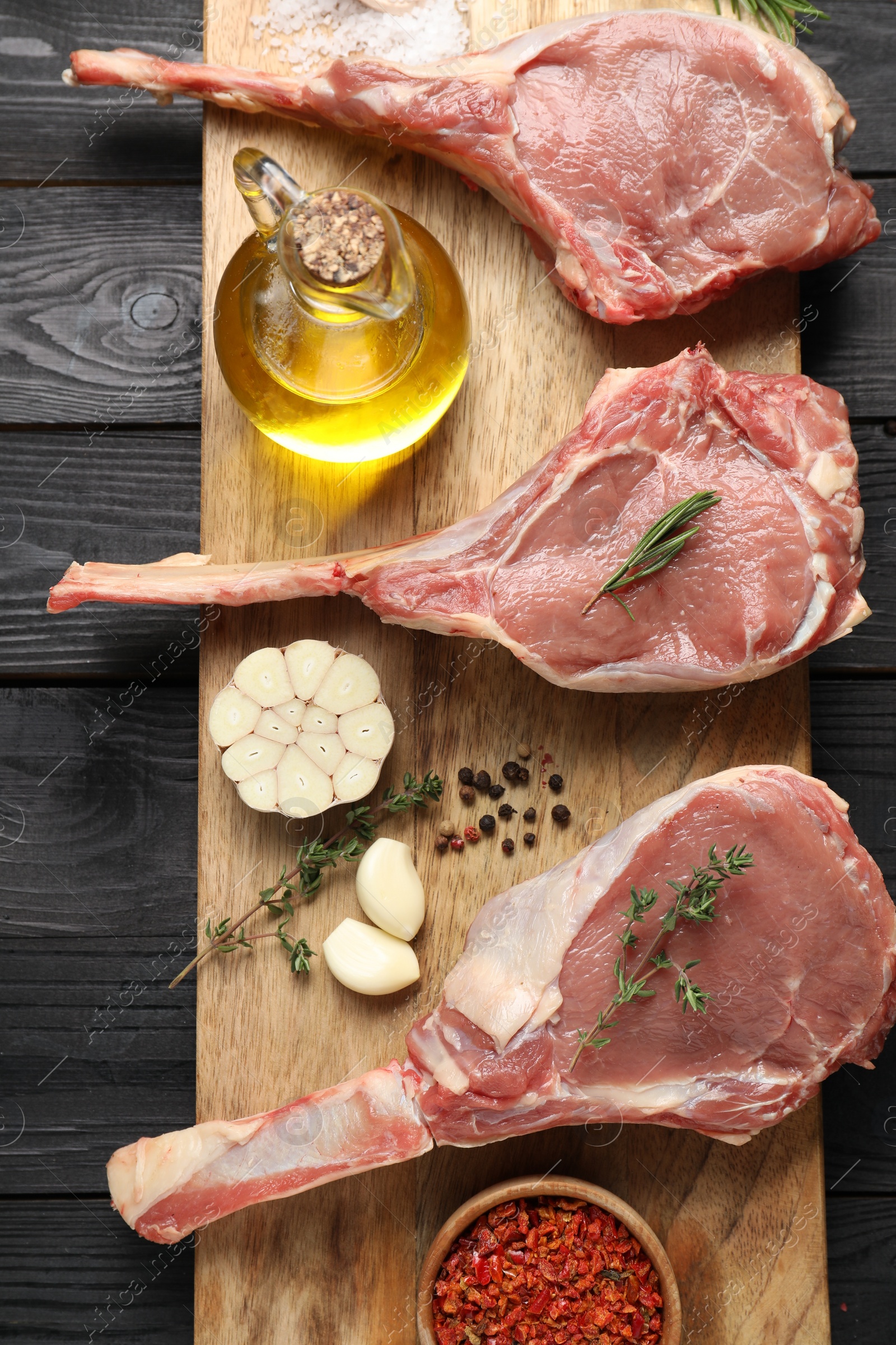 Photo of Fresh tomahawk beef cuts, spices and oil on black wooden table, top view