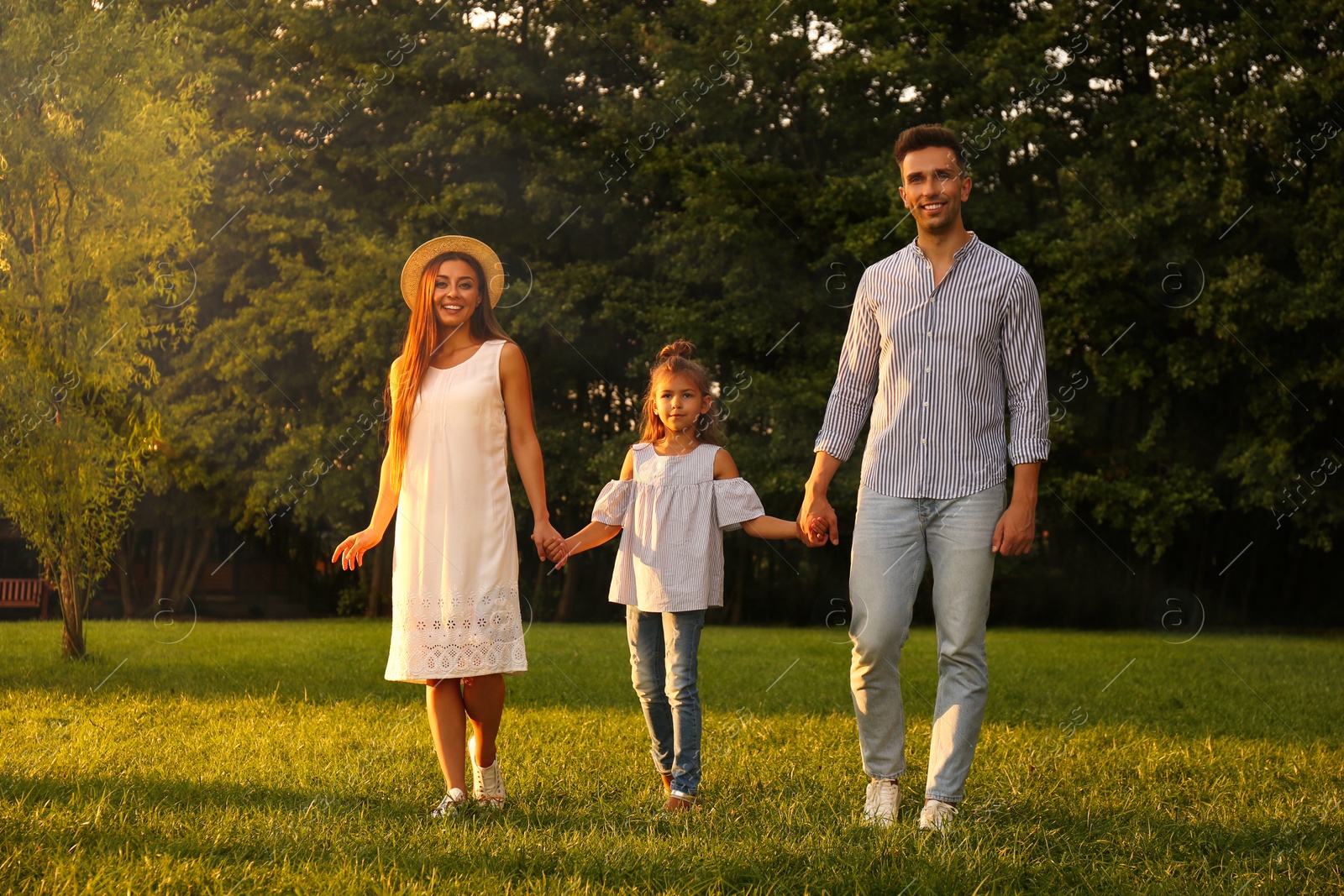 Photo of Little girl and her parents holding hands in park. Happy family