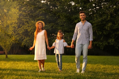 Little girl and her parents holding hands in park. Happy family